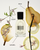 Perfume bottle labeled with floral, pear, cedar, caramel, and vanilla elements on a white background