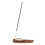 A single incense stick stands upright in a curved, polished brown wooden holder on a plain white background.