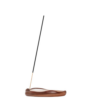 A single incense stick stands upright in a curved, polished brown wooden holder on a plain white background.