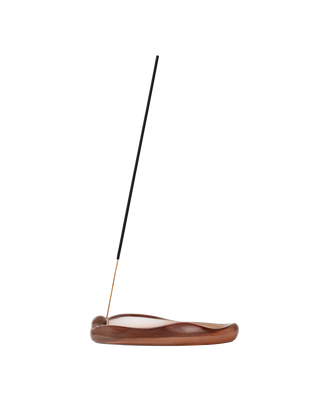 A single incense stick stands upright in a curved, polished brown wooden holder on a plain white background.